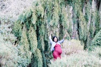 a pregnant woman posing under a willow tree