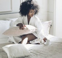 a woman in a white robe sitting on a bed holding a cup of coffee