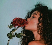 a woman with curly hair smelling a rose