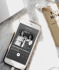 a phone with a podcast app on it next to a book and earphones