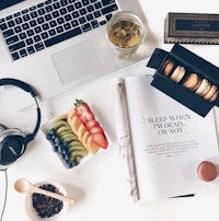 a desk with a laptop, headphones, fruit, and a book